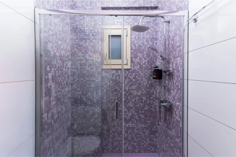 Close-up of a modern shower cabin with purple mosaic tiles, a rain shower head, and sliding glass doors at Ria's Apartment in Agios Nikolaos.