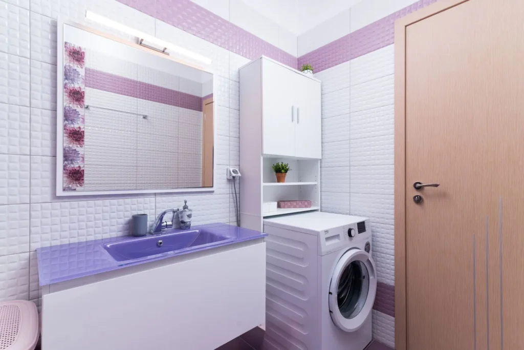 Modern bathroom vanity with a purple sink, illuminated mirror, and a Beko washing machine at Ria's Apartment in Agios Nikolaos.