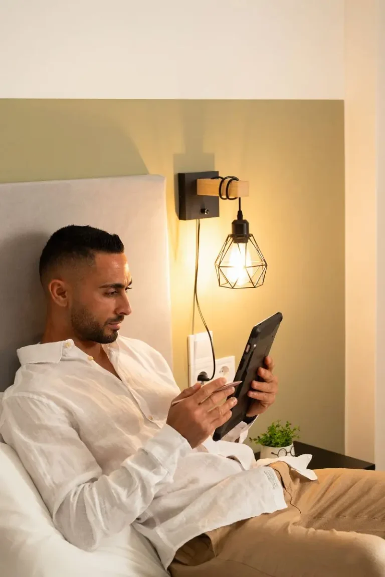A guest relaxing in bed with a tablet under warm bedside lighting at Ria's Apartment in Agios Nikolaos.