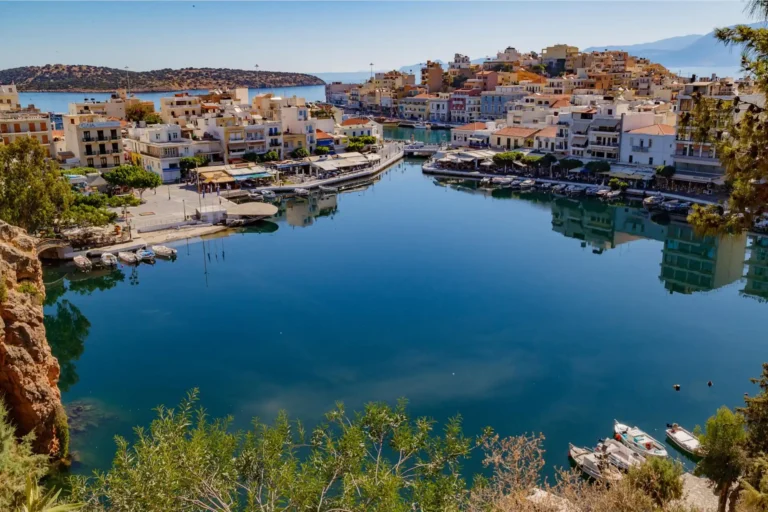 Πανοραμική θέα της Λίμνης Βουλισμένης στον Άγιο Νικόλαο Κρήτης με παραδοσιακές βάρκες, καφετέριες και τα χαρακτηριστικά βράχια.