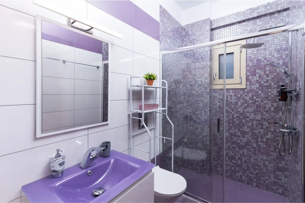 Modern second bathroom with a glass walk-in shower, purple mosaic tiles, a purple sink, and a large mirror at Ria's Apartment in Agios Nikolaos.