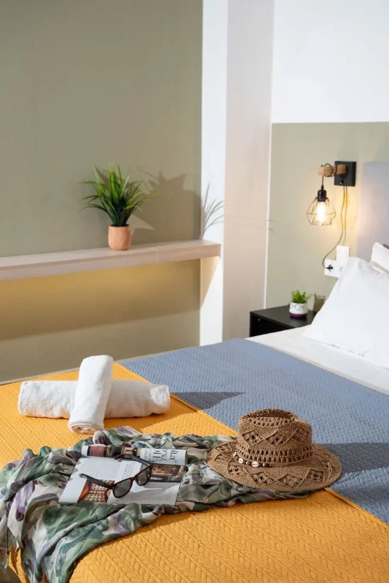 A wide interior view of the modern second double bedroom at Ria's Apartment in Agios Nikolaos, showcasing the colorful bedding, accent wall, and wood-look tile flooring.