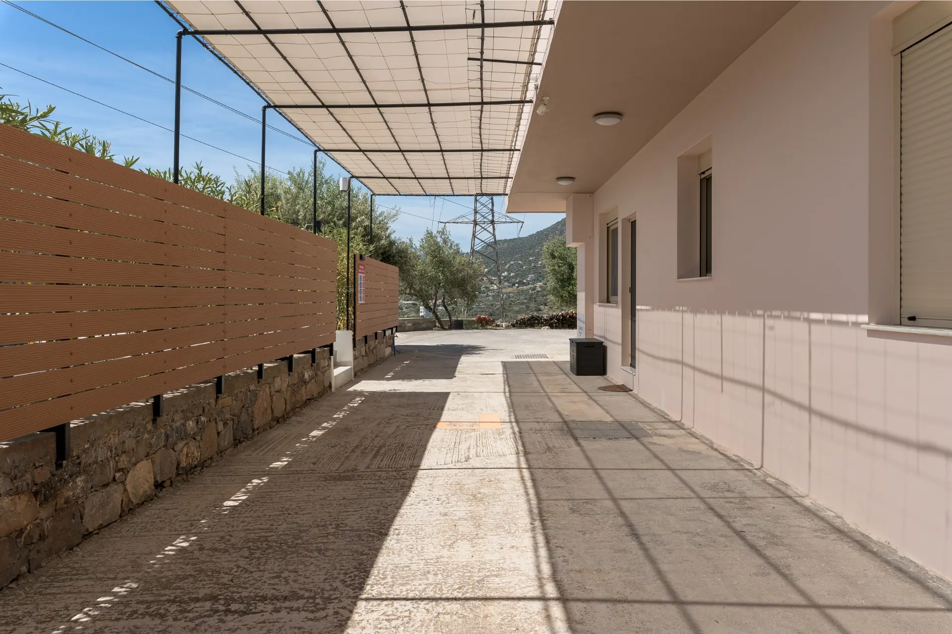 View of the entrance and private parking area at Ria's Apartment, featuring a shaded driveway and stone fencing.