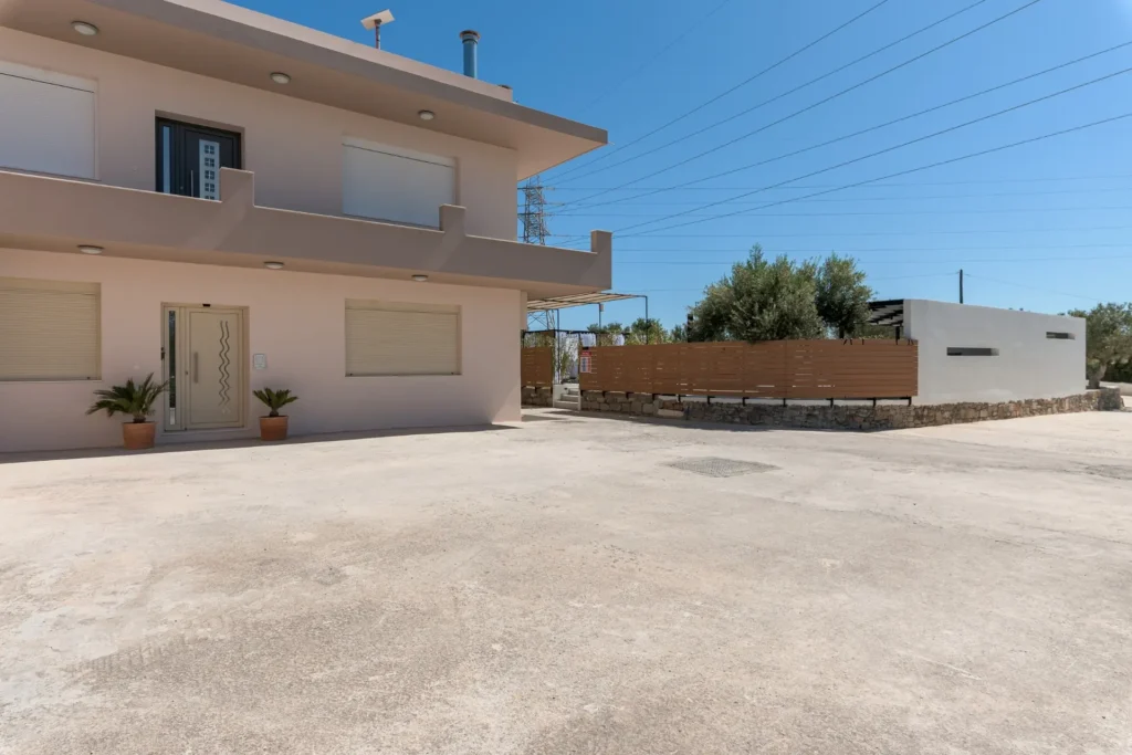 The exterior facade of Ria's Apartment featuring the spacious courtyard, modern fencing, and building entrances during daylight.