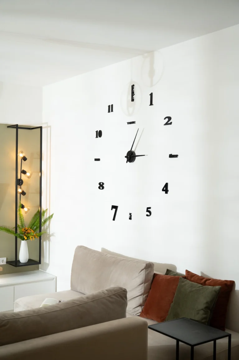 The living room at Ria's Apartment featuring a large sofa with decorative pillows, a striking minimal wall clock, and contemporary lighting.