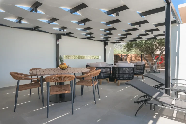 Modern outdoor dining set with a wooden table and wicker chairs next to a comfortable lounge area, under a stylish pergola at Ria's Apartment.