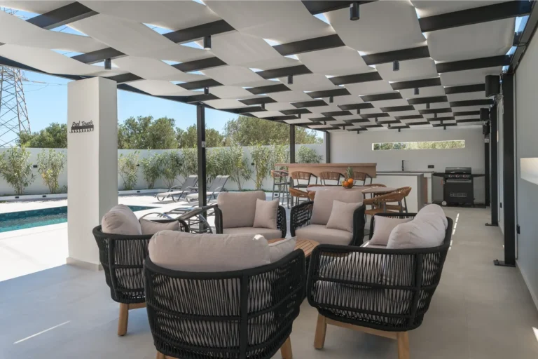 Comfortable outdoor lounge with gray armchairs under a pergola, overlooking the pool and the fully equipped BBQ area at Ria's Apartment.