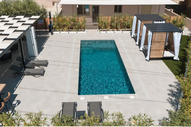 Top-down view of the rectangular swimming pool at Ria's Apartment, surrounded by sun loungers, luxury cabanas, and a shaded pergola area.