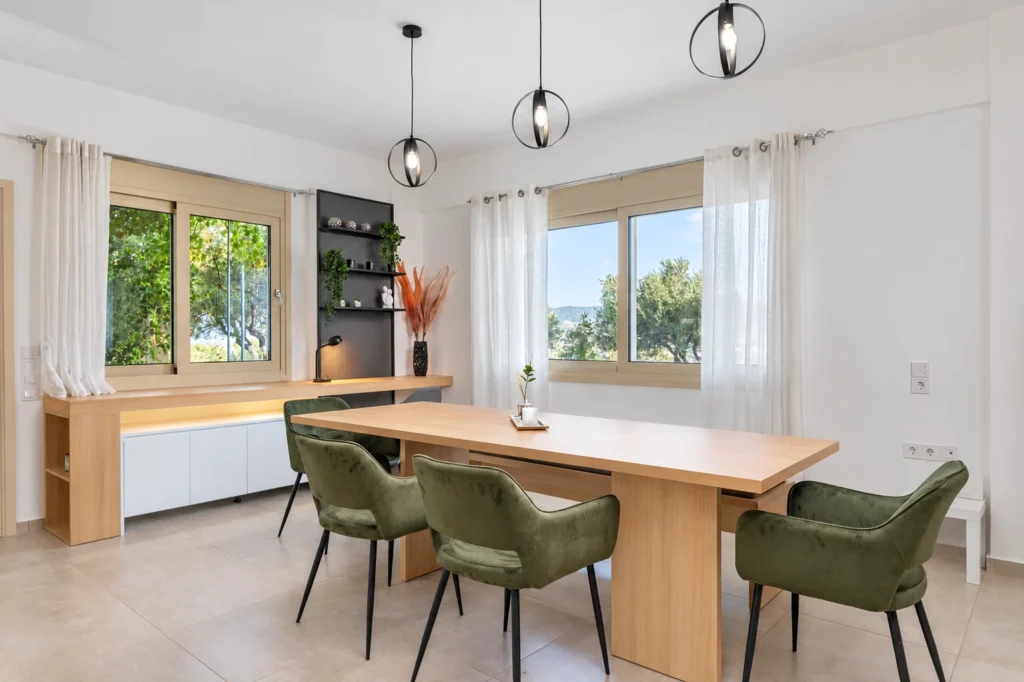 Bright, modern dining room with a large wooden table and green velvet chairs at Ria's Apartment in Agios Nikolaos.
