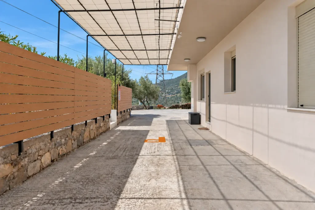 View of the entrance and private parking area at Ria Oasis Residence, featuring a shaded driveway and stone fencing.