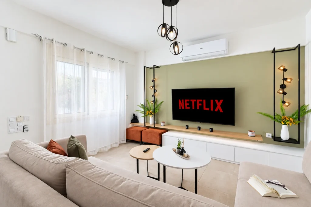 Wide view of modern living room at Ria's Apartment in Agios Nikolaos, showing comfortable sofas, tile floors, and Netflix TV.