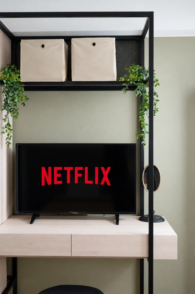 A television screen displaying the Netflix logo, set on a modern wooden desk with a black metal frame at Ria Oasis Residence.