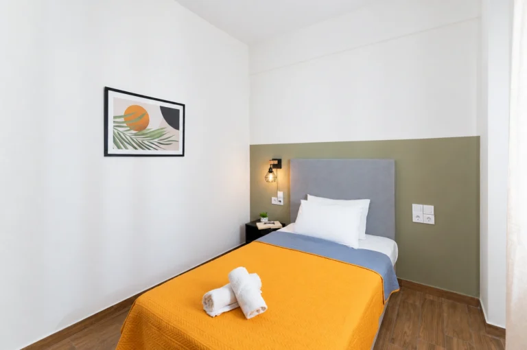 A modern single bed with yellow bedding and a framed tropical wall art print in the third twin bedroom at Ria Oasis Residence in Agios Nikolaos.